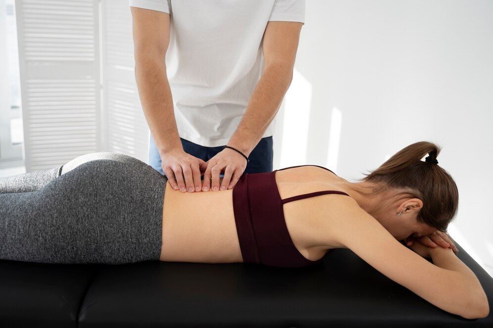 Chiropractor performing a lower back adjustment on a woman lying face down on a treatment table